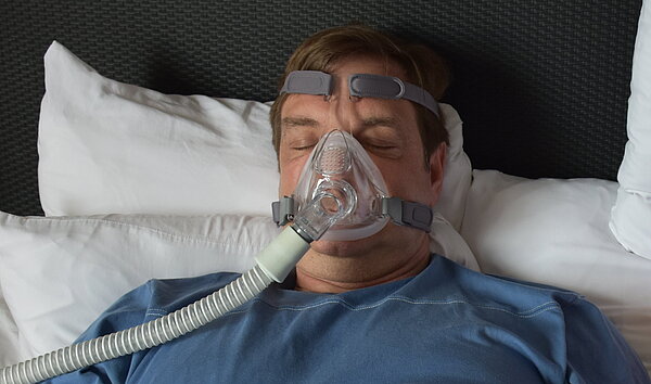 Im Bett: Er trägt eine CPAP-Maske, sie wird dadurch beim Schlafen gestört.