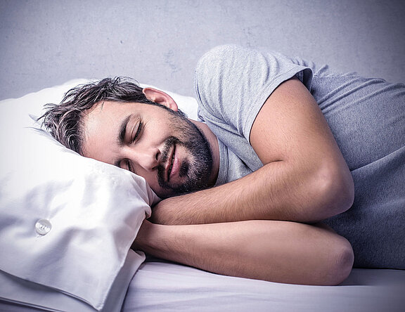 Mann schläft im Bett. Gesunder Schlaf ist wichtig für Körper und Geist  