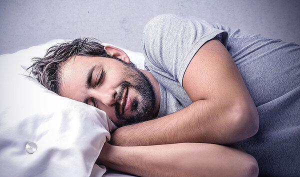 Mann schläft im Bett. Gesunder Schlaf ist wichtig für Körper und Geist