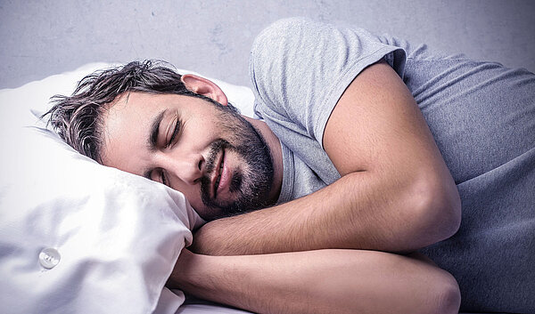 Mann schläft im Bett. Gesunder Schlaf ist wichtig für Körper und Geist