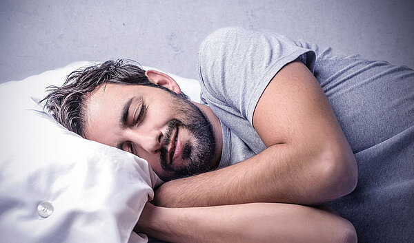 Mann schläft im Bett. Gesunder Schlaf ist wichtig für Körper und Geist