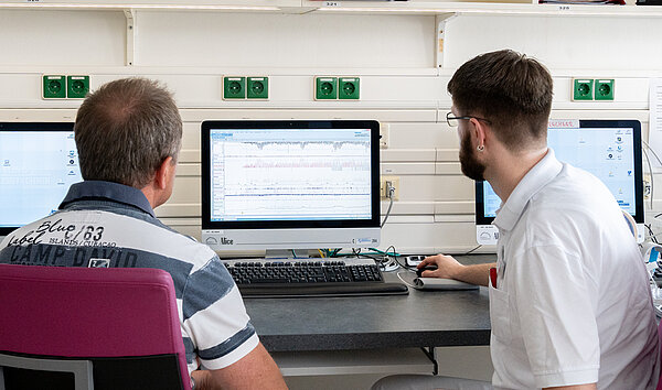 Patient und Arzt sitzen vor einem PC. Auswertung im Schlaflabor