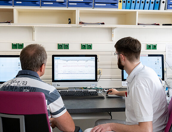 Patient und Arzt sitzen vor einem PC. Auswertung im Schlaflabor