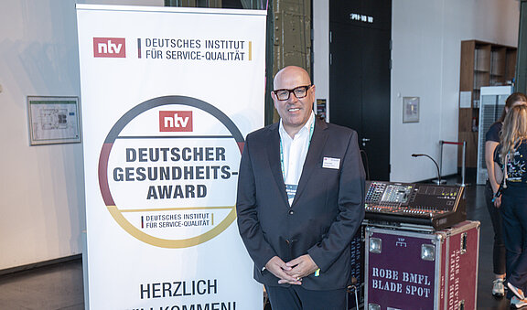 Andreas Henke, Senior Vice President und  Managing Director Europe von Inspire Medical Systems Europe GmbH, vor dem Schild „Deitscher Gesundheits-Award"  