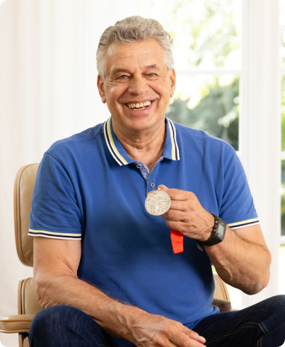 Fotografie von Inspire Nutzer Jürgen Hingsen, der im Stuhl sitzt und stolz seine Olympiamedaille in der Hand hält.