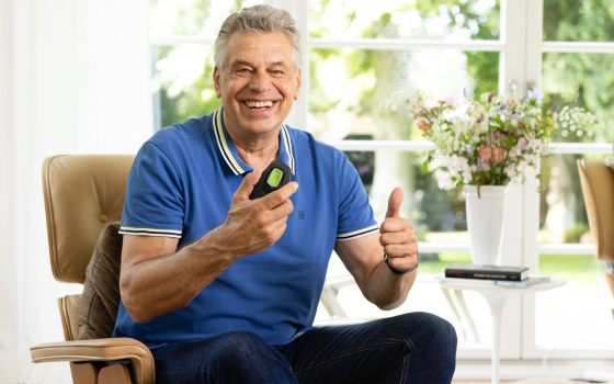 Foto von Inspire Nutzer Jürgen Hingsen, der zufrieden die Fernbedienung des Zungenschrittmachers in der Hand hält und mit der anderen Hand den Daumen hoch zeigt. 